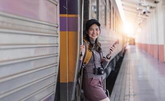 ung asiatisk kvinna i modern tåg station kvinna backpacker passagerare väntar för tåg på tåg station till gå på Semester. foto