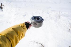 min hand innehar de pott och jag gröt mot de bakgrund av de snö. matlagning på en vandra i de berg, en pott i de hand av en turist, camping redskap. aluminium pott. foto