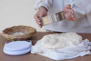 närbild hand innehar durkslag, deg mjöl för framställning bröd eller pizza, korg, skala på cookng tabell. begrepp, matlagning. kök livsstil. framställning mat. bageri. kärlek matlagning foto