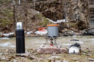 porslin för camping på de bakgrund av de flod, en plats för utomhus- rekreation, camping Utrustning, termos, vattenkokare, pott, gas brännare, camping gas. foto