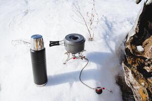 redskap för matlagning på en vandra, camping Utrustning står på de snö i vinter. laga mat de soppa i en kastrull på en brännare. foto