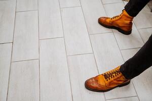 de kille bär eleganta orange skor. två ben är på de golv. herr- fötter är skodd i klassisk äkta läder stövlar. foto