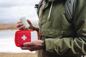 rulla av elastisk bandage i de hand av en mänsklig turist, röd först hjälpa utrustning med mediciner, röd korsa väska, behandling av skador i resa foto