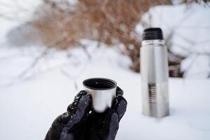 en kopp av varm te från en termos. dryck kaffe i natur. metall termisk råna tillverkad av stål. en flaska den där behåller värme. picknick redskap, camping utrustning. foto