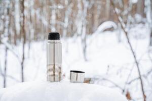 en kopp av varm te från en termos. dryck kaffe i natur. metall termisk råna tillverkad av stål. en flaska den där behåller värme. picknick redskap, camping utrustning. foto