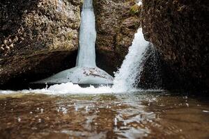 en vattenfall falls på de sida av de klippa, is hänger över de vatten, ett underjordisk grotta med en vattenfall, en vår översvämning i de berg, ett underjordisk sjö. foto