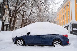 de bil är begravd under en lager av snö. tung snöfall i de stad. de Utrustning står under en snödriva. konsekvenser av en vinter- orkan. foto