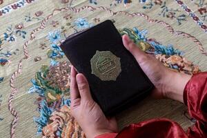 hand av en muslim kvinna innehav de quran med indonesiska översättning foto