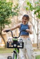 Lycklig ung asiatisk kvinna i tillfällig kläder njut av ridning cykel på de parkera för rekreation foto