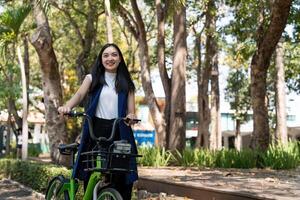 eco vänlig, Lycklig livsstil asiatisk skön ung affärskvinna ridning cykel gå till kontor arbete på stad gata med cykel i morgon- foto