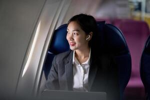 framgångsrik ung asiatisk företag kvinna sitter i flygplan stuga plan och arbetssätt från var som helst. flygande på först klass foto