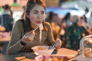 resande asiatisk kvinna njut av äter nudel på natt marknadsföra. traditionell chiang mai thailand gata mat. foto