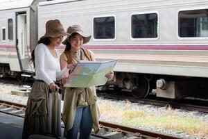 resa begrepp. flicka vän ha på sig hatt innehav Karta ha väska och bagage. kvinna resande väntar tåg på tåg station foto