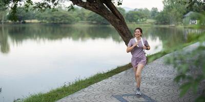 kvinna aktiva asiatisk kvinna i sportkläder lyssnande till musik medan löpning eller joggning i de parkera i de morgon- foto
