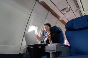 framgångsrik ung asiatisk företag kvinna sitter i flygplan stuga plan och arbetssätt från var som helst. flygande på först klass foto