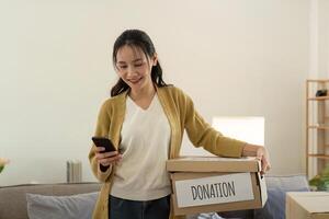 donation begrepp. kvinna asiatisk innehav en donera låda med full av kläder. kvinna innehav kläder donera låda. kläder i låda för begrepp donation och återanvändning återvinna foto