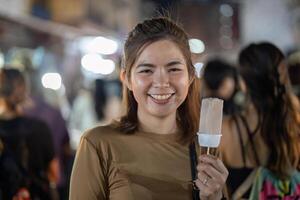 Lycklig ung skön kvinna äter en traditionell thai is grädde i de gata mat foto