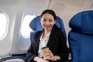 porträtt av en leende framgångsrik asiatisk affärskvinna eller kvinna entreprenör i formell kostym i en plan sitter i en företag klass sittplats under flyg foto