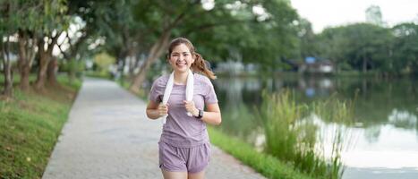 kvinna aktiva asiatisk kvinna i sportkläder lyssnande till musik medan löpning eller joggning i de parkera i de morgon- foto