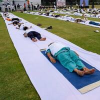 ny delhi, Indien, juni 21, 2023 - grupp yoga övning session för människor på yamuna sporter komplex i delhi på internationell yoga dag, stor grupp av vuxna delta yoga klass i cricket stadion foto