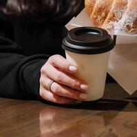 kvinna innehav en råna av kaffe och en croissant foto