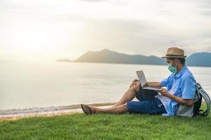 man bär mask med bärbar dator på stranden havet och man resa semester phuket sandlåda thailand är frihet livet ekonomiskt foto