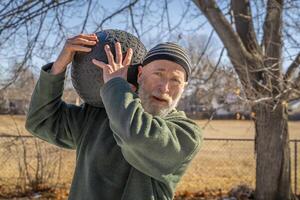 senior man är utövar med en tung, 50 lb, slam boll i hans bakgård, solig vinter- dag foto