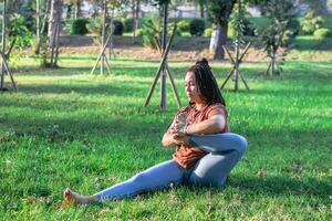 skön ung kvinna med lång afrikansk flätor är håller på med yoga utanför i en parkera. begrepp av friska livsstil. foto
