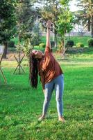 skön europeisk kvinna med lång afrikansk flätor. kvinna är håller på med yoga övning utanför i en parkera. foto