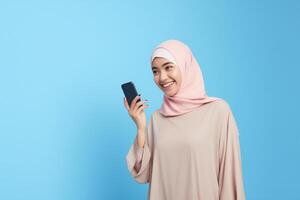 ai genererad söt ung asiatisk flicka i hijab innehav en smartphone i främre av en vibrerande blå bakgrund foto