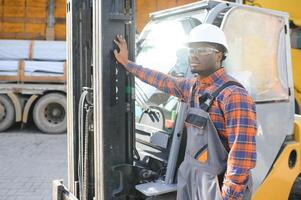 porträtt av en Lycklig afrikansk amerikan manlig arbetstagare körning gaffeltruck på arbetsplats foto