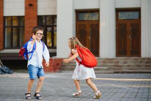 Lycklig barn gå tillbaka till skola. elev av primär skola gå studie med ryggsäck utomhus. barn gå hand i hand. början av lektioner. först dag av falla. pojke och flicka från elementärt studerande. foto