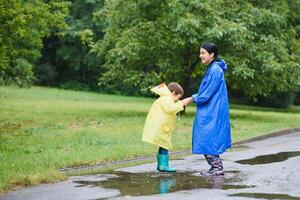 mamma och son i regnrockar ha roligt tillsammans i de regn. begrepp av familj semester och Lycklig barndom. foto