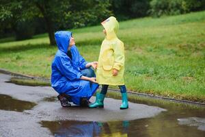 mamma och son i regnrockar ha roligt tillsammans i de regn. begrepp av familj semester och Lycklig barndom. foto