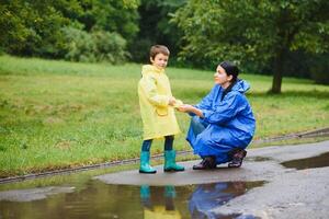 mor med son gående i parkera i de regn bär sudd stövlar foto