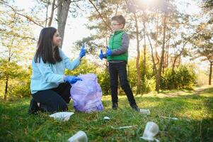 mamma lär henne son till rena upp skräp i natur. en kvinna tar bort plast flaskor i en väska. de ämne av miljö- förorening förbi sopor. foto