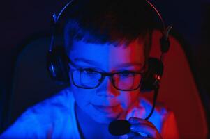 barn uppkopplad sändningar dator spel, pojke strömmar i hörlurar på rgb belysning bakgrund foto