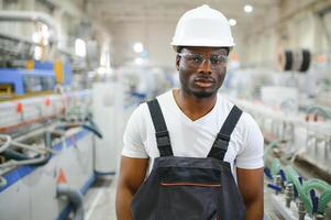 porträtt av afrikansk amerikan manlig ingenjör i enhetlig och stående i industriell fabrik foto