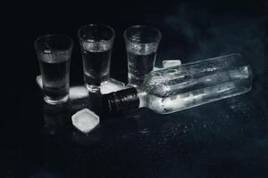 närbild se av flaska av vodka med glasögon stående på is på svart. foto