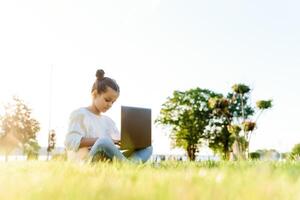 barn med läsplatta pc utomhus. liten flicka på gräs med dator foto