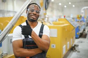 porträtt av afrikansk amerikan manlig ingenjör i enhetlig och stående i industriell fabrik foto