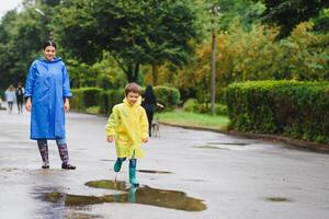 mor och barn, pojke, spelar i de regn, bär stövlar och regnrockar foto