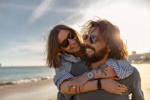 Lycklig romantisk par i kärlek kramas medan gående längs de strand på solig dag foto