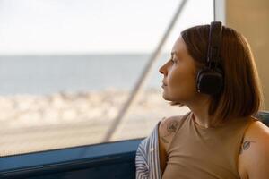 kvinna i hörlurar medan reser i offentlig transport och ser se utanför de fönster foto