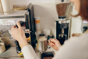 stänga upp av kvinna Barista skummar mjölk på en kaffe maskin för framställning cappuccino eller latte foto