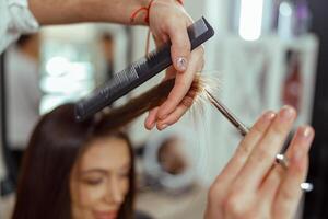 stänga upp av kosmetolog händer innehav en hår strå medan skärande hår av kvinna foto