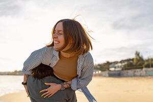 smilng par i kärlek lura runt om medan gående längs de strand på solig blåsigt dag foto