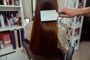 närbild av hårstylist pensling lång och elegant brun hår av kvinna klient på skönhet salong foto