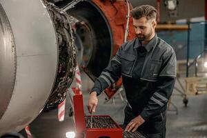 manlig flygplan mekaniker använder sig av instrument låda i hangar foto