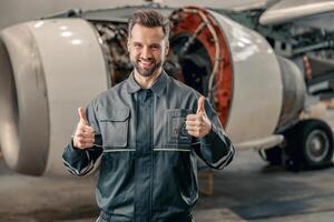 glad flygbolag mekaniker som visar godkännande gest i hangar foto